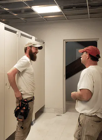 Photo of two toilet partition installers talking next to a set of Elite Series bathroom stalls