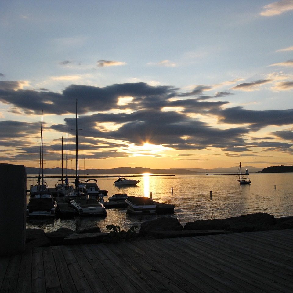 Photograph of sunset over a Vermont bay, clouds and sailboats.