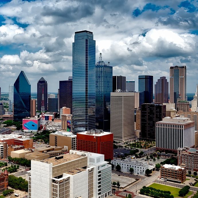 Photograph of Dallas, Texas cityscape with skyscrapers, clouds, blue sky.